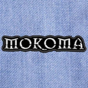 以下が含まれることがあります： 「MOKOMA」という単語がギザギザのフォントで刺繍された黒と白のワッペンです。