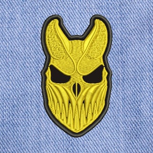 Op de afbeelding: Een gele geborduurde patch van een schedel met hoorns en een tandenrij. De schedel is omrand met zwart.