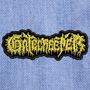 May include: Black and yellow embroidered patch with the text "Dethklok" in a stylized font.