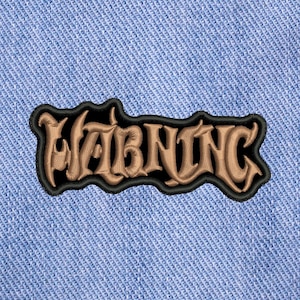 May include: An embroidered patch featuring the word WARNING in a stylized, tan-colored gothic font with a thick black outline. The patch is stitched onto a light blue denim fabric background with a visible diagonal weave pattern throughout the material.