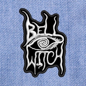 Puede incluir: Parche bordado en blanco y negro con el texto "Bell Witch" y un ojo estilizado con una espiral en su interior.