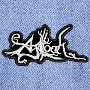 Puede incluir: Parche bordado en blanco y negro con la palabra "Arkwood" en una fuente gótica estilizada. El parche tiene un borde negro y está sobre un fondo de mezclilla azul claro.