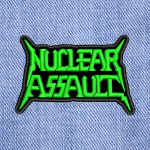Puede incluir: Parche bordado verde con las palabras "NUCLEAR ASSAULT" en contorno negro.