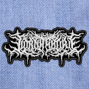 May include: White embroidered patch with the text "WORMROT" in a black gothic font on a black background.