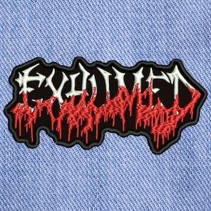 以下が含まれることがあります： 「EVIL」という単語が赤い滴る文字で書かれた黒と白の刺繍パッチ。パッチは青いデニムの背景の上にあります。