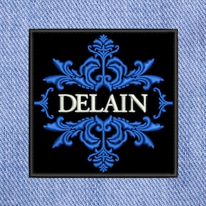 Puede incluir: Parche bordado en blanco y negro con un diseño floral azul y la palabra "DELAIN" en letras blancas.
