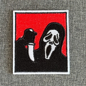 May include: Embroidered patch featuring the Ghostface mask from the Scream horror film series. The patch has a red background with a black figure holding a knife. The mask is white with black details, and the patch is outlined in white.