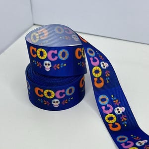 May include: A roll of blue ribbon printed with the word "COCO" in various colours, plus skull and floral patterns. This ribbon is suitable for crafts or gift wrapping, and has a Day of the Dead theme.