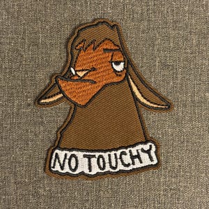 May include: Embroidered patch featuring a brown cartoon goat with a grumpy expression. The patch has a white border and the words "NO TOUCHY" in black lettering. The goat's face is a lighter shade of brown.