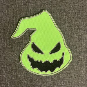 May include: A neon green patch featuring a stylized, grinning face with black eyes and mouth. The patch has a gray border and is likely for a Halloween or spooky-themed project. The design is reminiscent of a character from a popular animated film.
