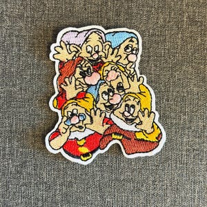 May include: Embroidered patch featuring the seven dwarfs from Snow White. The patch has a white border and depicts the dwarfs in various colours, including red, yellow, blue, and purple. The dwarfs are smiling and waving.