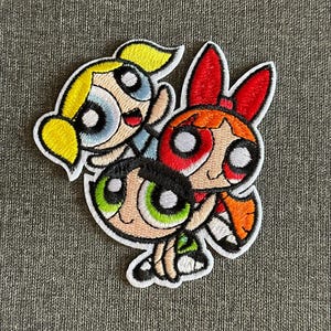 Könnte beinhalten: Gestickter Aufnäher mit den Powerpuff Girls. Der Aufnäher zeigt die drei Zeichentrickfiguren mit ihren charakteristischen Farben: Blossom in Rot, Bubbles in Blau und Buttercup in Grün. Der Aufnäher hat einen weißen Rand.