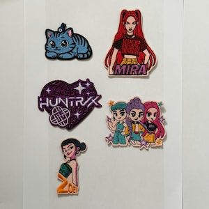 Może przedstawiać: Kolekcja haftowanych naszywek z postaciami z kreskówek i tekstem. Projekty obejmują niebieskiego kota, kobietę z rudymi włosami i napisem "KPOP DEMON HUNTERS MIRA", fioletowe serce z napisem "HUNTRX", grupę trzech dziewczyn i kobietę z napisem "ZOEY".