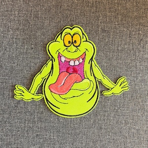 May include: A neon green embroidered patch featuring a cartoon character with a wide open mouth and a long pink tongue. The character has yellow eyes and a black outline. The patch is on a gray background.