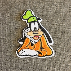May include: Embroidered patch featuring Goofy, a Disney cartoon character. The patch depicts Goofy in his classic orange shirt, green hat, and white gloves. The patch is outlined in black and white.