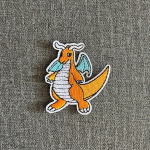 May include: Embroidered patch featuring a cartoon dragon in shades of orange, white, and blue. The dragon has a white outline and is set against a gray background. The patch is likely for clothing or accessories.