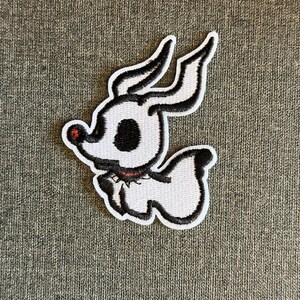 Op de afbeelding: Geborduurde patch met Zero, de spookhond uit The Nightmare Before Christmas. De patch is wit met zwarte contouren en details, waaronder Zero's grote oren, zwarte oog en rode neus. Een zwarte kraag met rode accenten maakt het ontwerp compleet.