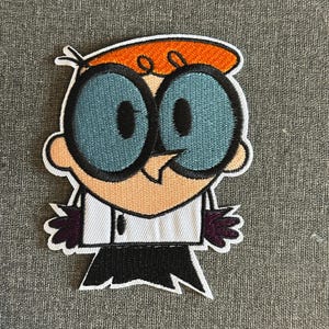 May include: Embroidered patch featuring Dexter from the animated series Dexter's Laboratory. The patch depicts Dexter with his signature large blue eyes, orange hair, and a white lab coat. The patch is outlined in black and has a white border.