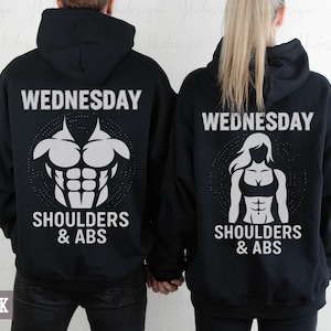 Puede incluir: Sudaderas con capucha negras con gráficos blancos. Una sudadera presenta un gráfico de físico masculino con el texto "WEDNESDAY SHOULDERS & ABS". La otra sudadera muestra un gráfico de físico femenino con el mismo texto. La palabra "BLACK" está en la parte inferior.