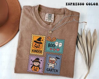 May include: Espresso-colored t-shirt with a Halloween-themed design. The design features four postage stamp-style graphics with a pumpkin, ghosts, a witch, and a mummy bear. The shirt has a crew neck and a Comfort Colors tag.