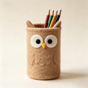 Peut inclure: Un porte-crayons cylindrique en feutrine en forme de hibou avec un corps beige, deux yeux circulaires blancs à pupilles noires, un petit bec jaune et deux petites touffes d'oreilles. Quatre crayons de couleur rouge, vert, jaune et bleu sont dedans.