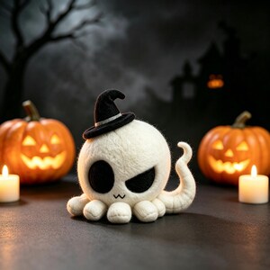 May include: A needle-felted white octopus figurine with a black witch hat, featuring large black eye patches and a small stitched mouth. The creature has multiple rounded tentacles and one curved tentacle extending upward from its body.