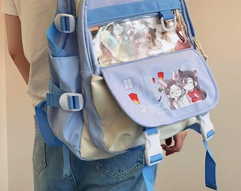 May include: A light blue and cream-colored backpack with multiple compartments and adjustable straps. The front flap features a clear window and a colorful illustration of anime characters. The backpack has white and blue accents.