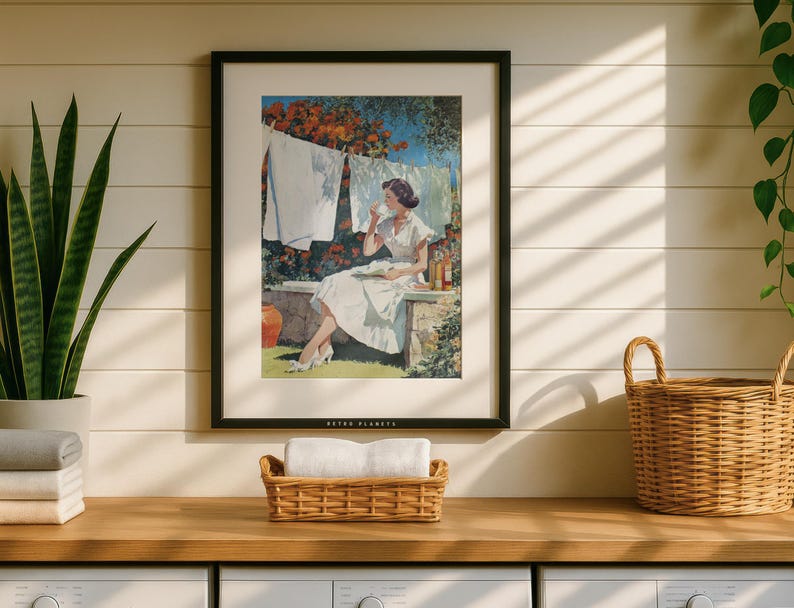 Vintage laundry print in black frame above counter with wicker baskets and plants, sunlit wall.