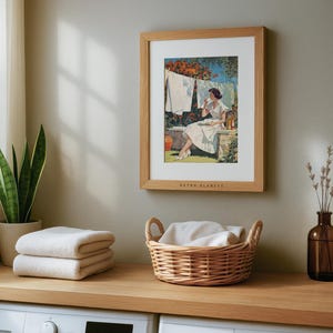 Mid-century laundry wall art in light oak frame above laundry counter with folded towels.