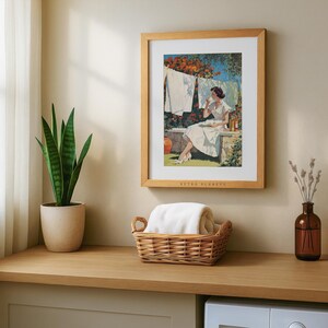 Mid-century laundry artwork in oak frame above wicker laundry basket with indoor plants.