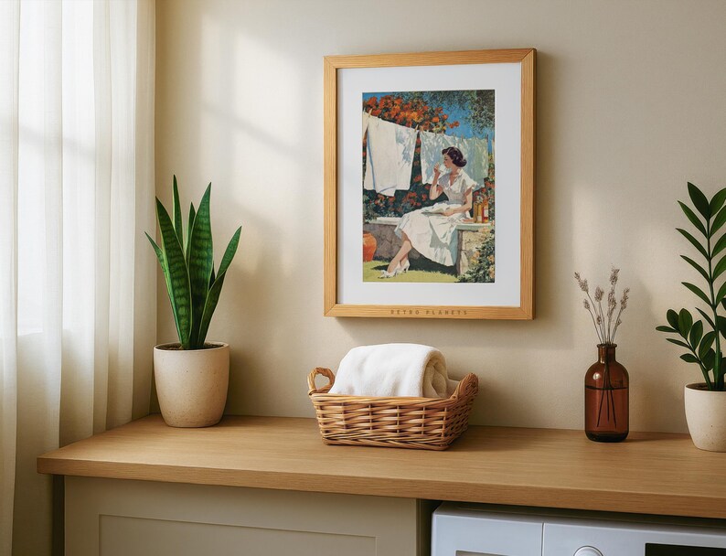Mid-century laundry artwork in oak frame above wicker laundry basket with indoor plants.