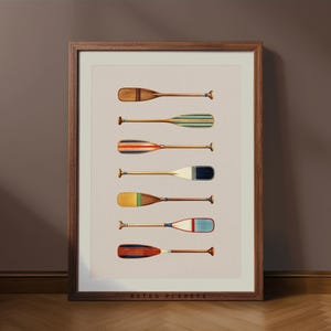 Puede incluir: Una impresión enmarcada que presenta siete remos de estilo vintage en varios colores y diseños. Los remos están dispuestos verticalmente sobre un fondo neutro, dentro de un marco de madera. La impresión tiene una estética retro, que evoca temas náuticos y deportes acuáticos.