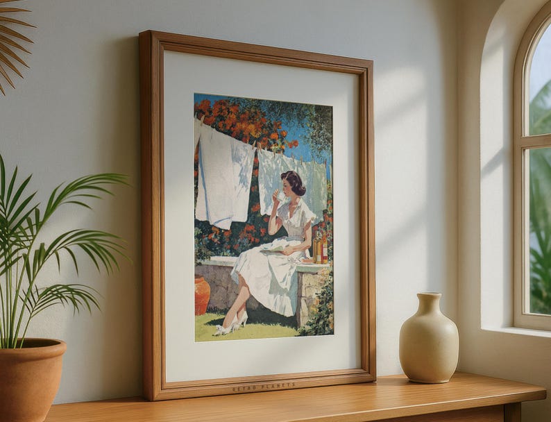 Retro laundry wall art framed in oak by sunlit window with ceramic vase and potted palm.