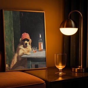 May include: A framed art print depicts a golden retriever wearing sunglasses and a red cap, smoking a cigarette, and sitting at a table with a drink and a bottle. A gold-toned lamp and a glass are on a dark surface.