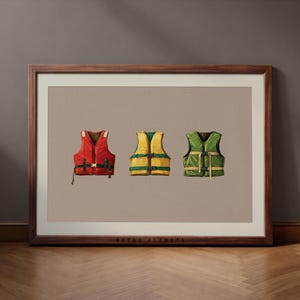 Puede incluir: Impresión enmarcada con tres chalecos salvavidas en rojo, amarillo y verde. Los chalecos se muestran sobre un fondo neutro, cada uno con hebillas y correas visibles. La impresión está en un marco de madera.