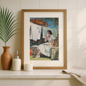 Retro clothesline wall art framed in oak on tiled bathroom shelf with candle and palm leaf.