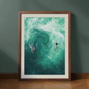 May include: A framed art print depicting two people swimming in turquoise ocean water. The artwork is in a brown wooden frame and set against a dark green wall. The text "RETRO PLANETS" is printed at the bottom of the frame.