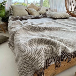 Può includere: Una coperta in tessuto beige e marrone con frange su una struttura letto in legno. La coperta ha un motivo geometrico ed è piegata sul letto.