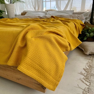 Może przedstawiać: Żółty koc wafelkowy drapowany na drewnianym stelażu łóżka. Koc jest miękki i przytulny, idealny do dodania odrobiny ciepła i stylu do każdej sypialni.