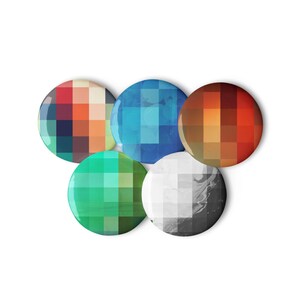 Puede incluir: Cinco botones redondos y coloridos con un diseño pixelado. Los botones están dispuestos en círculo, con el botón azul en la parte superior, el botón naranja a la derecha, el botón gris en la parte inferior derecha, el botón verde en la parte inferior izquierda y el botón rojo a la izquierda.