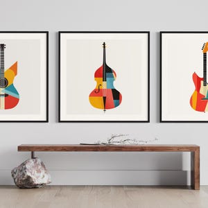 Op de afbeelding: Drie ingelijste prints van muziekinstrumenten met een geometrisch ontwerp. De prints tonen een gitaar, een bas en een elektrische gitaar. De instrumenten zijn allemaal in tinten rood, geel, blauw en zwart.