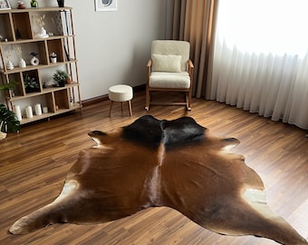Könnte beinhalten: Ein großer, unregelmäßig geformter Kuhfellteppich mit einem Farbverlauf von tiefem Schwarz an der Oberseite bis hin zu verschiedenen warmen Braun- und Beigetönen in der Mitte und an den Rändern, flach ausgelegt auf einem polierten Holzboden.