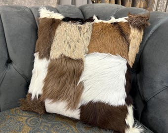May include: A brown, white, and tan patchwork throw pillow with a soft, furry texture. The pillow is made of different pieces of animal hide sewn together.