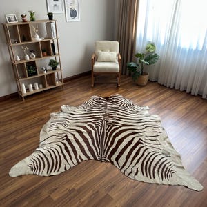 May include: A large, irregularly shaped area rug featuring a distinct zebra-inspired pattern with dark brown stripes against a cream-coloured background. The rug is laid flat on a wooden floor, showcasing its natural hide-like silhouette and texture.