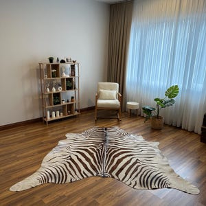 May include: A zebra-print rug with a brown and white pattern is the focal point. The rug is placed on a wooden floor. The room also features a wooden bookshelf, a rocking chair, and a potted plant. The room has a neutral colour palette.