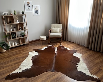 May include: A large, irregular-shaped cowhide rug featuring a natural pattern of deep brown and creamy white patches. The rug is laid flat on a dark wood-grain floor, showcasing the organic, asymmetrical silhouette and smooth texture of the hide.