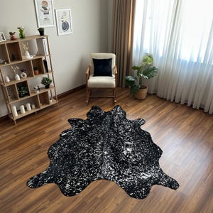 May include: A large, irregularly shaped cowhide rug featuring a speckled pattern of black and metallic silver. The rug lies flat on a wooden floor, showcasing a natural hide silhouette with a high-contrast, shimmering finish across its surface.