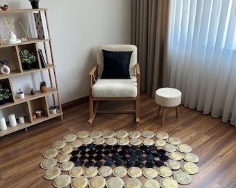May include: An oval area rug constructed from numerous circular discs arranged in concentric patterns. The center consists of dark black discs, while the outer perimeter is composed of metallic gold discs with a textured, shimmering finish.