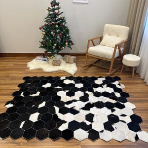 May include: A black and white cowhide rug featuring a geometric honeycomb design. The rug is composed of hexagonal tiles and is laid on a wooden floor. A Christmas tree with decorations and a rocking chair are visible in the background.
