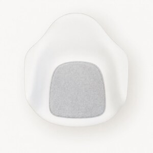 May include: A modern white chair with a rounded back and a gray, rectangular seat cushion. The chair is made of a smooth, glossy material and is set against a plain white background. The design is minimalist and contemporary.
